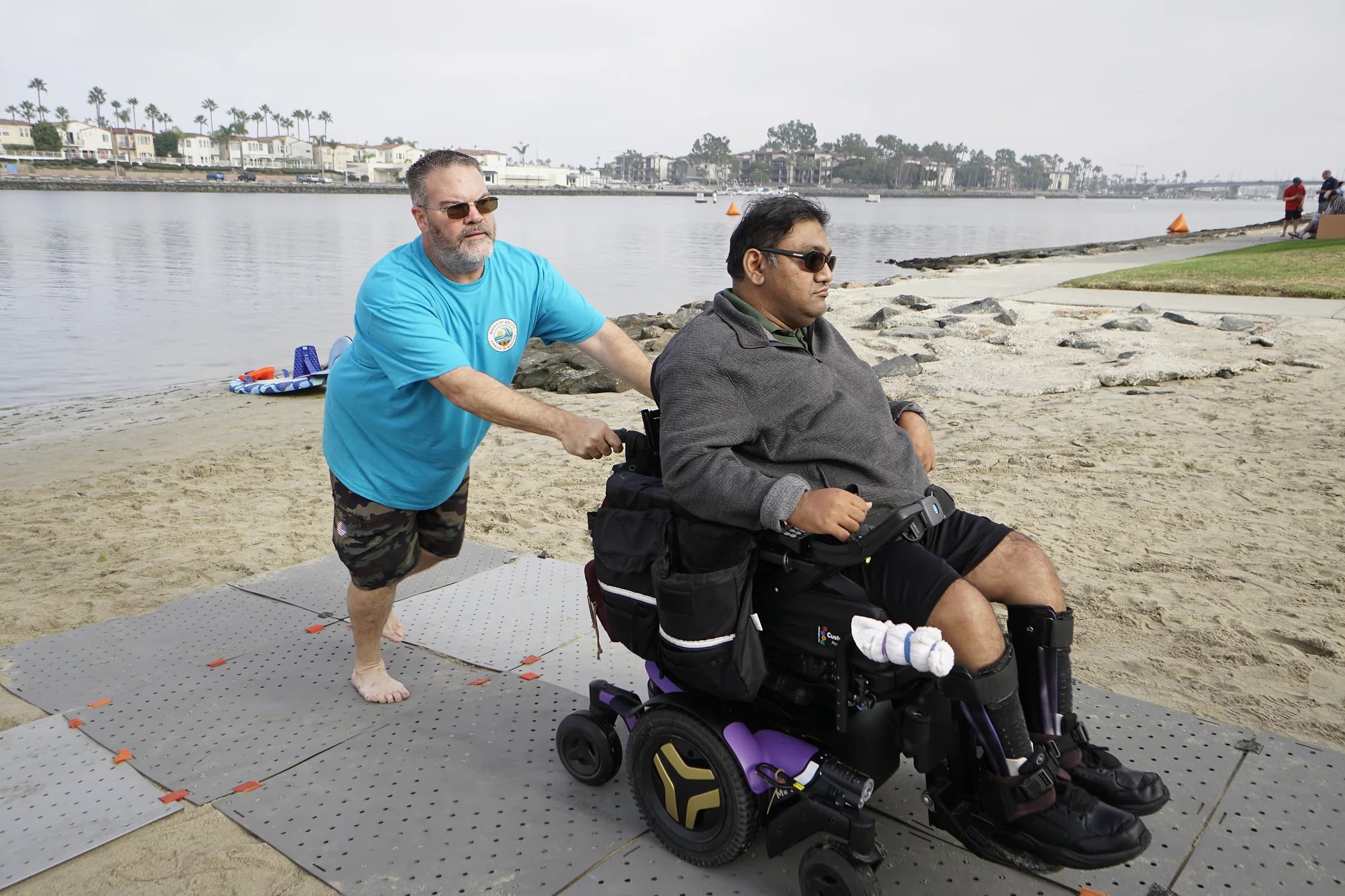 An AFF volunteer assisting a wheelchair user along the accessible beach pathway