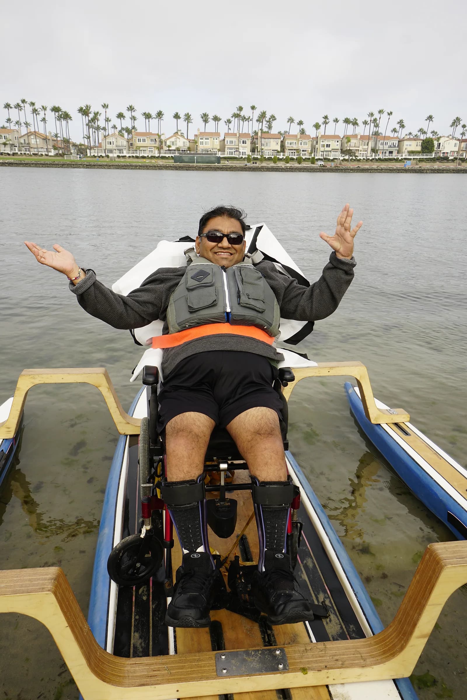 An adaptive paddler smiling with both arms raised while seated securely on an AFF board