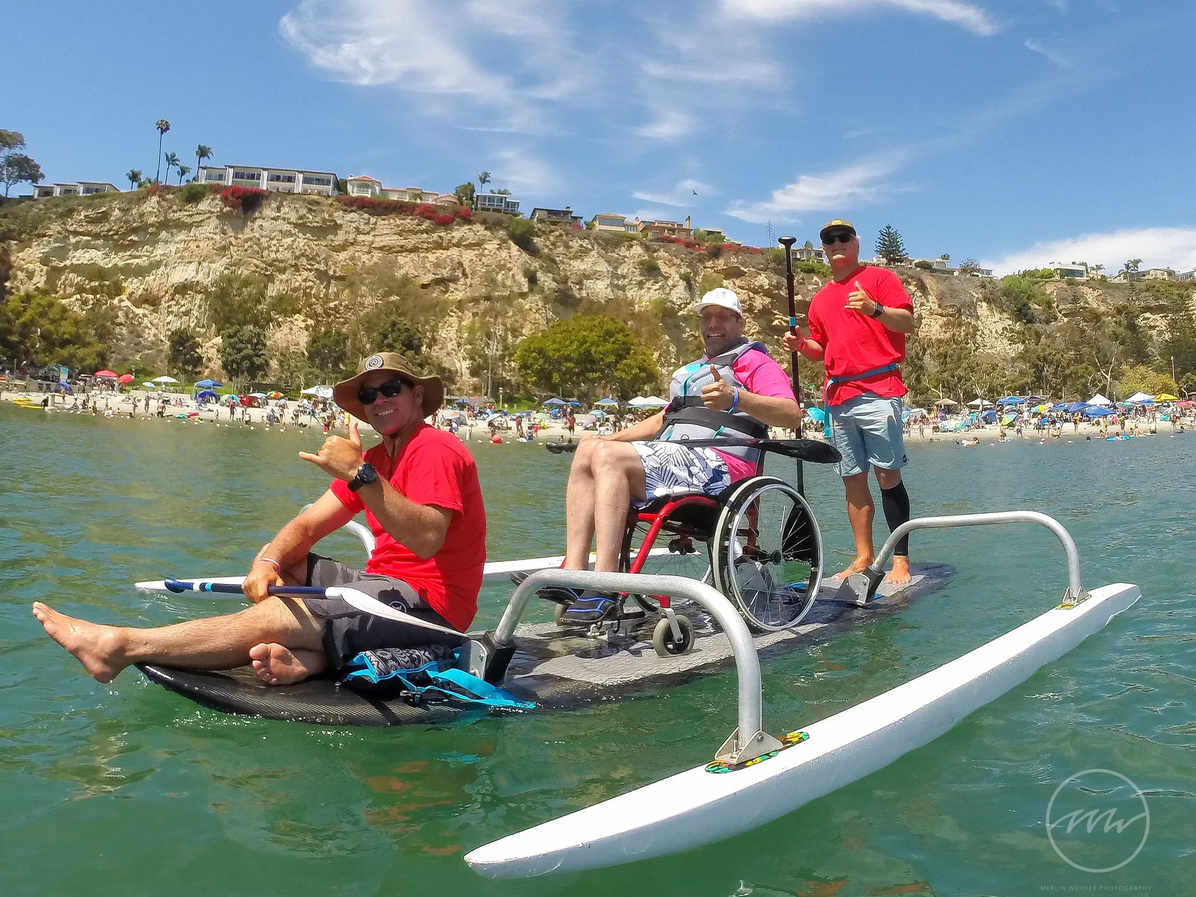A wheelchair user paddling an adapted board with two AFF volunteers on open water